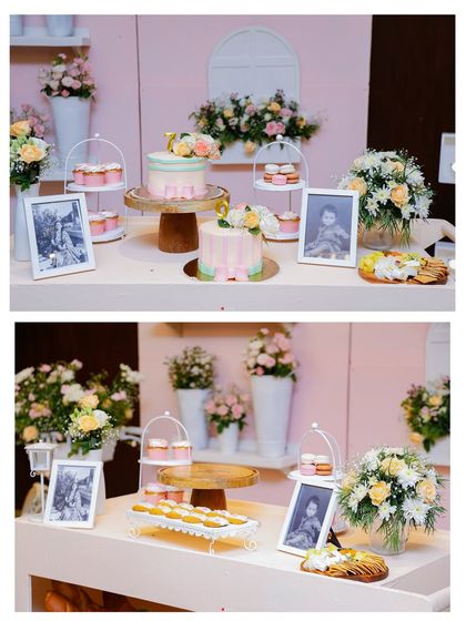 An elegant dessert table in pastel pink and white. The setup includes two beautiful cakes, cupcakes, and framed photos of the birthday child.