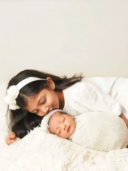 A quiet, tender moment as a big sister lays a gentle kiss on her sleeping newborn sibling. The all-white theme adds to the pure and innocent feel of the photo.