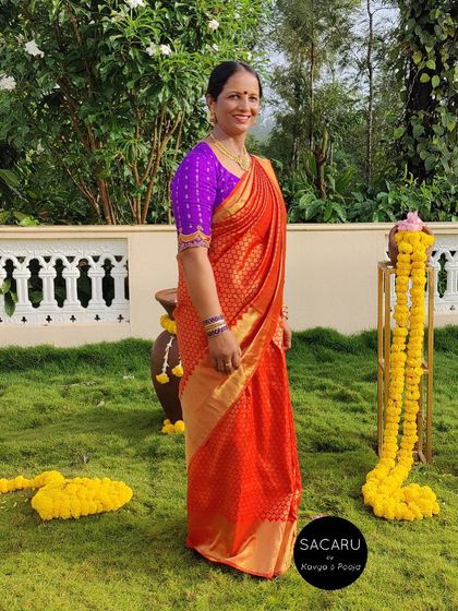 Contrast saree blouse styling on point. Our client wears a vibrant purple blouse with her orange Kanjeevaram saree for a festive look.