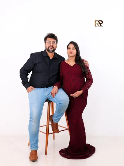 A classic and confident couple's portrait. The simple white background and their smart-casual attire result in a clean, modern, and stylish maternity photo.