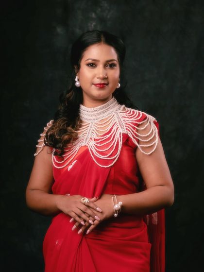 A regal portrait in a red saree, adorned with a statement pearl necklace. The dark, moody background makes the red and the pearls stand out, creating a look of pure elegance.