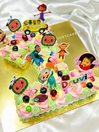A Cocomelon-themed number '1' cake for a first birthday. This pull-apart style cake is loaded with colorful characters and treats.