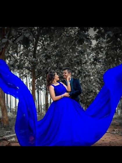 Using a color-pop effect, this photo highlights the vibrant royal blue of the gown against a monochrome forest background. The flowing train wraps around the couple, making them the center of this artistic shot.