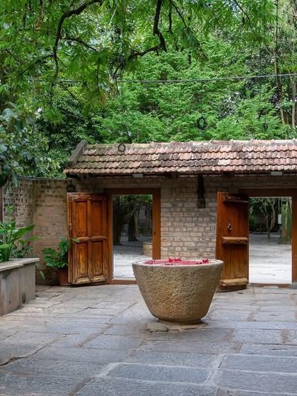 A stone courtyard featuring a large stone urn filled with water and petals, a classic element of South Indian welcome and decor.