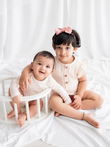 Siblings together. An older sister puts a loving arm around her baby brother in this sweet studio shot.