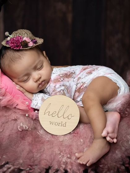 A close-up on the baby's face in the wreath basket, highlighting the cute little hat and the 'hello world' sign.