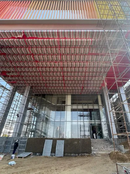 The entrance of an upcoming school in Gurugram under construction. The image shows the installation of colourful ceiling panels and the large glass facade, hinting at the bright and welcoming space to come.