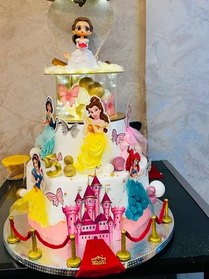 A truly magical multi-tier Disney Princess cake for a grand 5th birthday celebration. This design features a castle, a red carpet entrance, and beloved princesses like Belle, Ariel, and Cinderella, all brought together in one spectacular, edible creation.