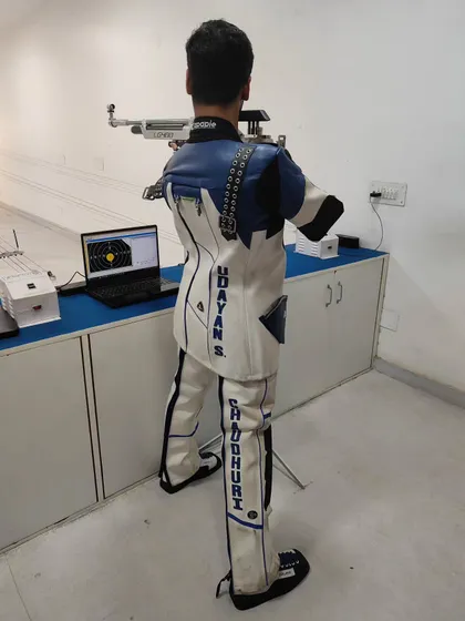The back of a shooter's custom-fitted jacket, highlighting the specialized gear that aids in stability and performance. This is 15-year-old Udayan during a training session. stance and form.