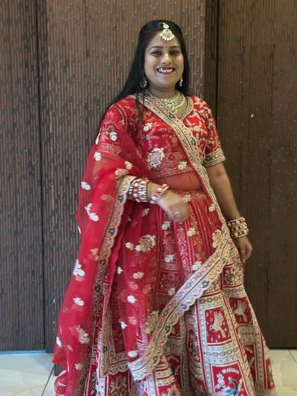 A smiling bride-to-be trying on a classic red wedding lehenga at our store. Notice the detailed floral and elephant motifs, a popular choice for traditional ceremonies.