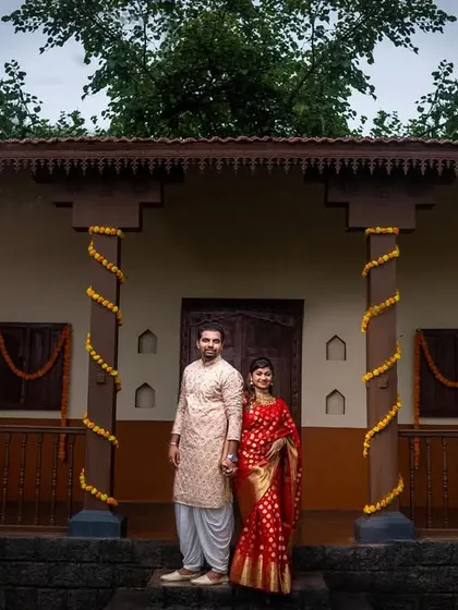 A wide shot of the couple at a heritage location, showcasing the grandeur of traditional Maharashtrian architecture.