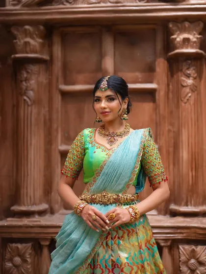 This portrait showcases a designer half saree against a beautifully carved wooden door. The setting adds a touch of architectural interest and complements the traditional outfit.