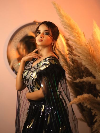 A confident and poised portrait. The model looks directly at the camera, showcasing her stunning makeup and the intricate design of her glamorous outfit.