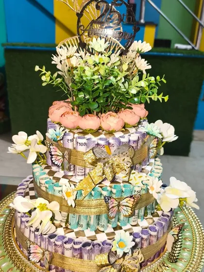 This is a three-tier cash cake I made for a 25th anniversary, built entirely from real currency notes. It's a unique way to gift money for a big milestone, decorated with flowers and a custom topper.