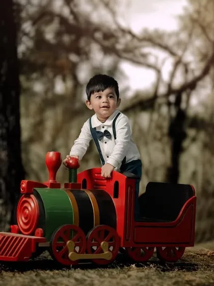 All aboard for adventure. This little boy looks ready to explore as he stands proudly on his toy train in the woods.