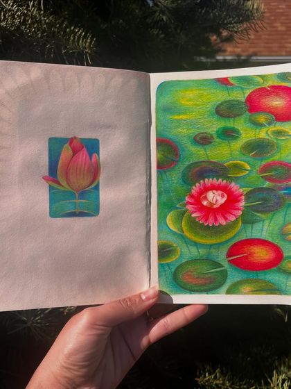 Holding the sketchbook open to the 'floating flower face' drawing.