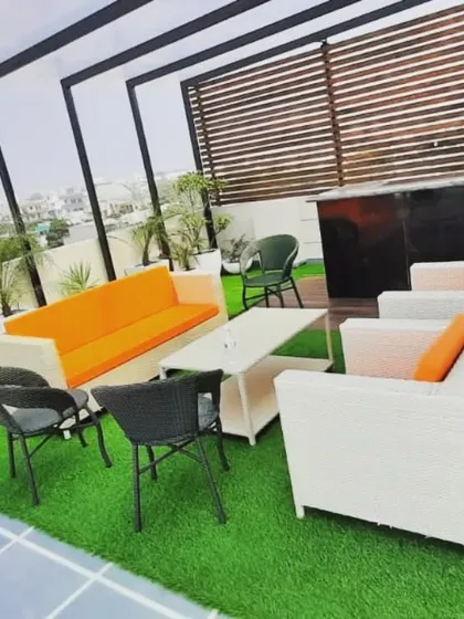A modern rooftop lounge with wicker sofas and chairs in contrasting colors, set under a sleek black pergola.