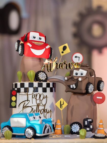 The amazing Disney Cars themed cake for Atharva's 5th birthday, featuring edible models of Lightning McQueen and Mater on a desert road.