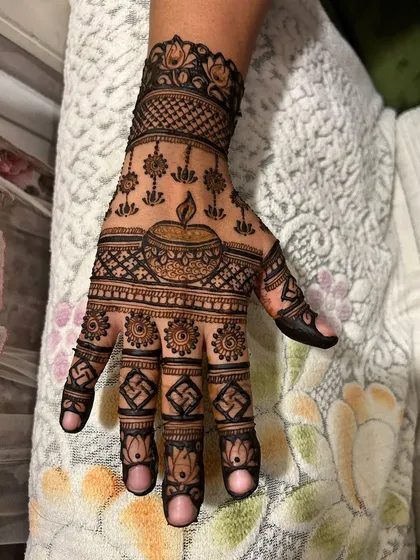 A perfect Diwali mehendi, with a brightly shining diya at its center. The design is complemented by auspicious swastika symbols and lotus patterns on the fingers.