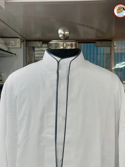 A white saya kurta with dark grey piping. This detail along the collar and placket gives the traditional garment a modern and charismatic look.