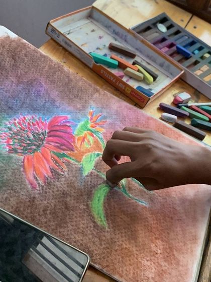 A student works with soft pastels to create a vibrant floral piece. The direct application of color with pastels is a uniquely tactile and enjoyable experience.