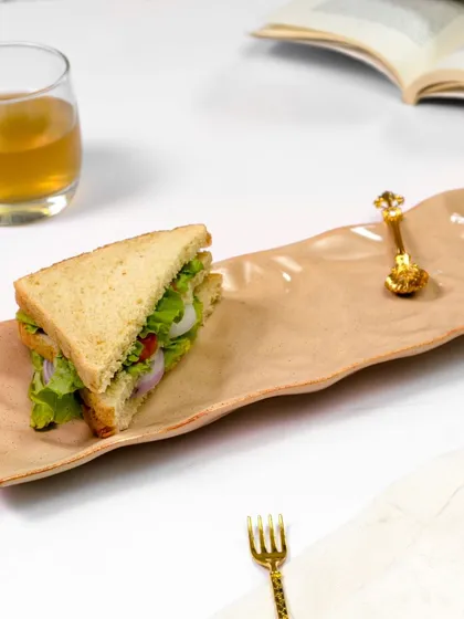 Another view of the ceramic platter, this time with the sandwich placed differently. The composition with a book and drink suggests a relaxing meal or a quiet break.