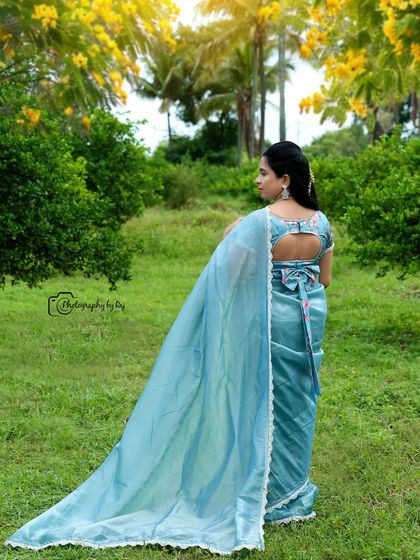 A beautiful back shot of a mother-to-be in a light blue saree, showing off the intricate blouse design and the flowing pallu.