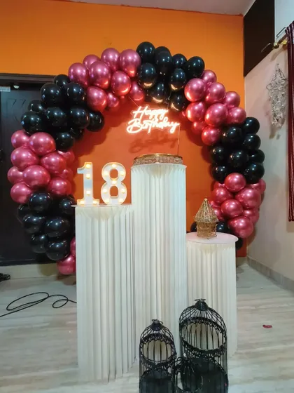 An 18th birthday is a huge milestone, and I create decor to match. This setup uses a bold black and metallic pink balloon ring, a neon sign, and a large light-up '18' to mark the special occasion.