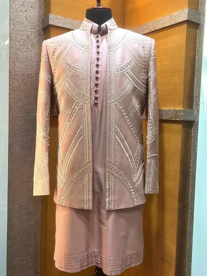 This luxurious silk sherwani in a soft pink hue features geometric embroidery and subtle mirror work, offering a modern take on royal attire.