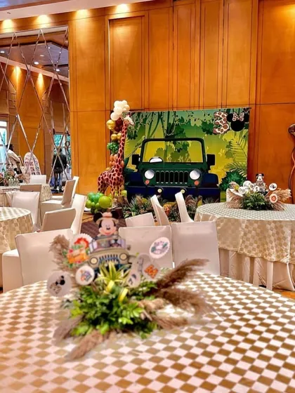 An overview of the jungle-themed party space, showing themed tablecloths and centerpieces. The safari jeep backdrop in the distance ensures the theme is carried throughout the entire venue.
