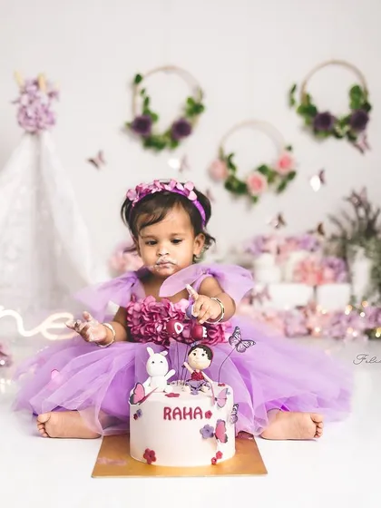 A magical first birthday cake smash. This little girl is exploring her beautiful butterfly cake in an enchanted purple garden.