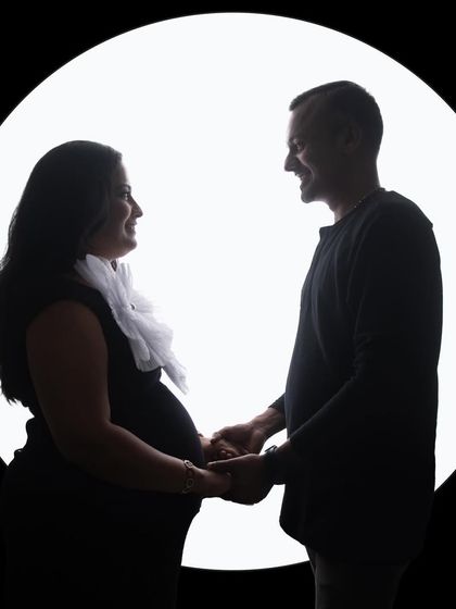 A sweet couple's silhouette against a circular light source, reminiscent of a full moon. Their happy expressions are just visible, adding a personal touch to the artistic shot.