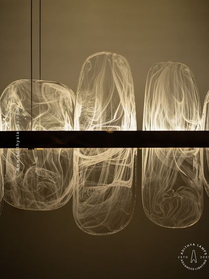 This linear pendant features organic, rounded glass elements with a beautiful white smoke effect inside. Suspended from a simple gold bar, it provides a soft, ethereal glow, ideal for creating a serene atmosphere over a dining table.