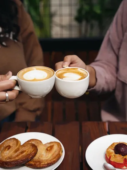 All I want this weekend is some good coffee and sweet treats. This shot captures a "cheers" moment between two friends over coffee, creating a relatable and happy cafe scene.