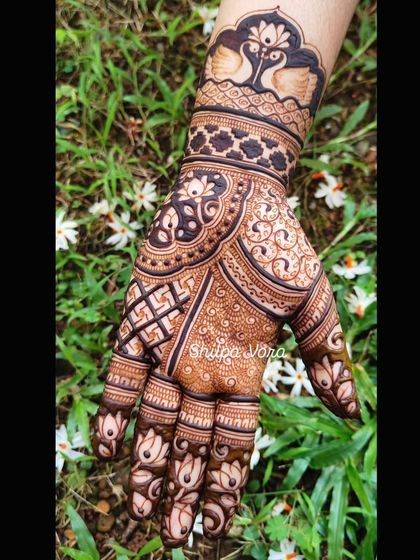 A single hand with a rich, dense design featuring peacocks and lotuses, set against a natural green background.