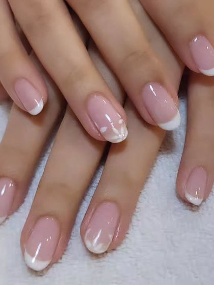 A classic French manicure on beautifully shaped natural nails. The accent nail features a delicate, translucent white flower for a touch of elegance.