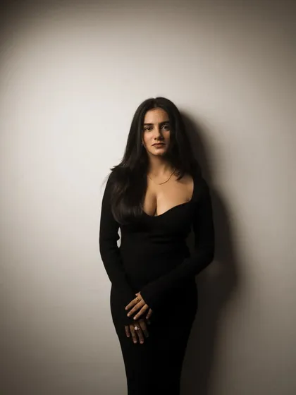 A simple, elegant studio portrait with a single light source creating a soft vignette. The focus is entirely on the subject's confident presence.