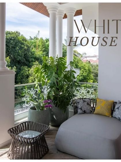 A serene balcony at "The White House" project, featuring classic columns and comfortable outdoor furniture. This space serves as a tranquil perch to enjoy views of the lush green canopy.