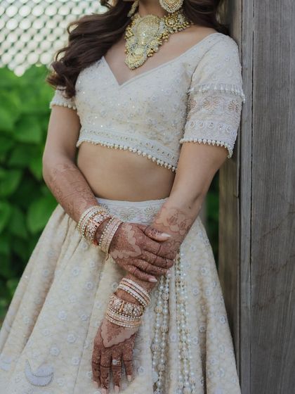 A mid-shot showing the details of Sheena's ivory lehenga, henna, and bangles. The soft, natural makeup look ensures that all elements of her bridal attire are in perfect harmony.
