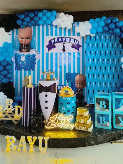 A detailed and exciting Boss Baby themed first birthday party. This setup includes a custom-printed backdrop, character cutouts, a balloon arch in theme colors, and personalized marquee letters spelling out the birthday boy's name.