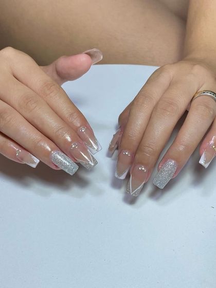 A perfect set for a bride. These long, coffin-shaped nails feature a glittery French manicure with a delicate V-shape and rhinestone accents.
