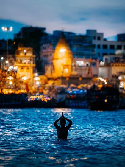 A lone devotee performs 'surya namaskar' in the holy Ganga at dawn, with the ancient city of Varanasi glowing in the background. This single frame captures the essence of faith and timelessness.