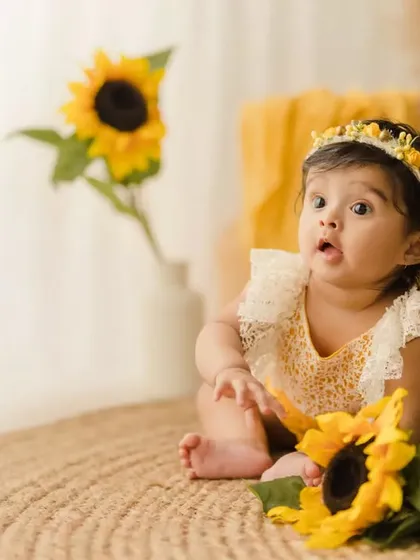 A curious baby girl during her sitter session, looking with wide eyes at a sunflower. These milestone shoots are perfect for capturing their budding personalities.