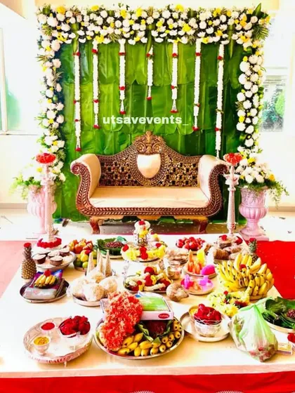 A beautiful baby shower setup with a banana leaf backdrop and a traditional golden divan. The foreground is filled with colorful fruits and sweets as part of the ceremony.