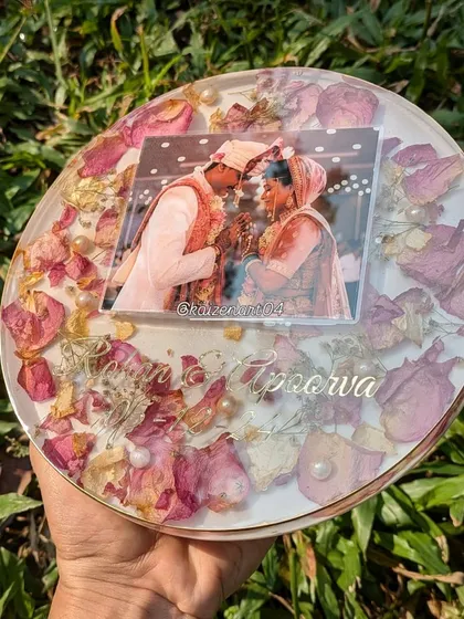 A circular 8-inch resin frame featuring beautiful pink rose petals and pearls. This design comes with a stand, making it a perfect addition to a side table or mantelpiece.