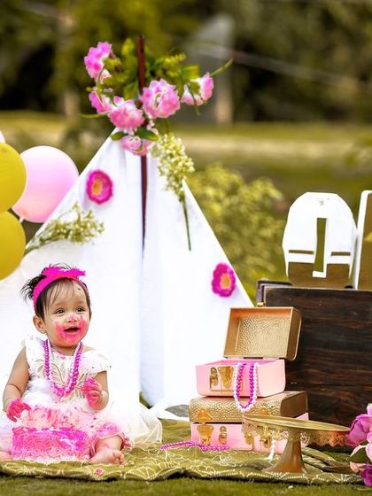 An outdoor cake smash session with a bohemian teepee setup. This little girl is enjoying her cake in a beautiful park setting, combining nature with celebration.