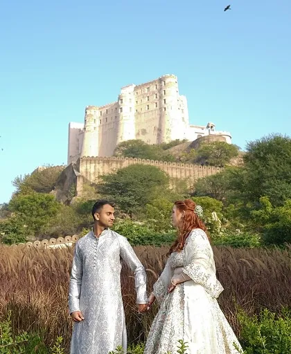A cross-cultural couple stands before the magnificent Alila Fort. I love planning weddings that bring together different traditions in a beautiful, harmonious celebration.