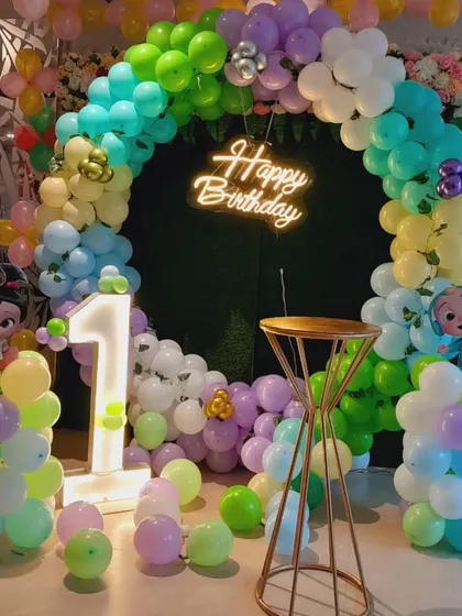 A Cocomelon first birthday party with a green artificial grass base. The decor includes a circular balloon arch and a light-up number '1'.
