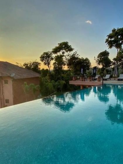 The sun sets over the infinity pool at a resort in Sakleshpur, reflecting the beautiful colors of the sky.