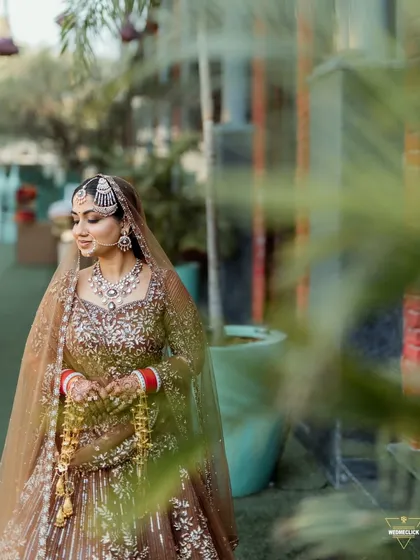 A candid portrait of the bride, capturing a moment of quiet reflection amidst the greenery. Her traditional attire and gentle smile are the focus.